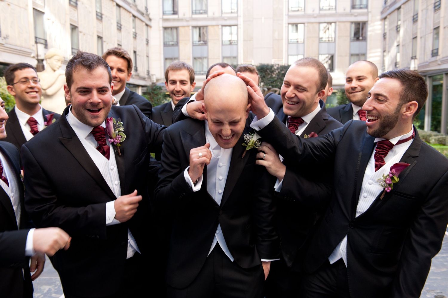 A group of formally dressed people in black suits and ties laugh together in a celebratory moment.