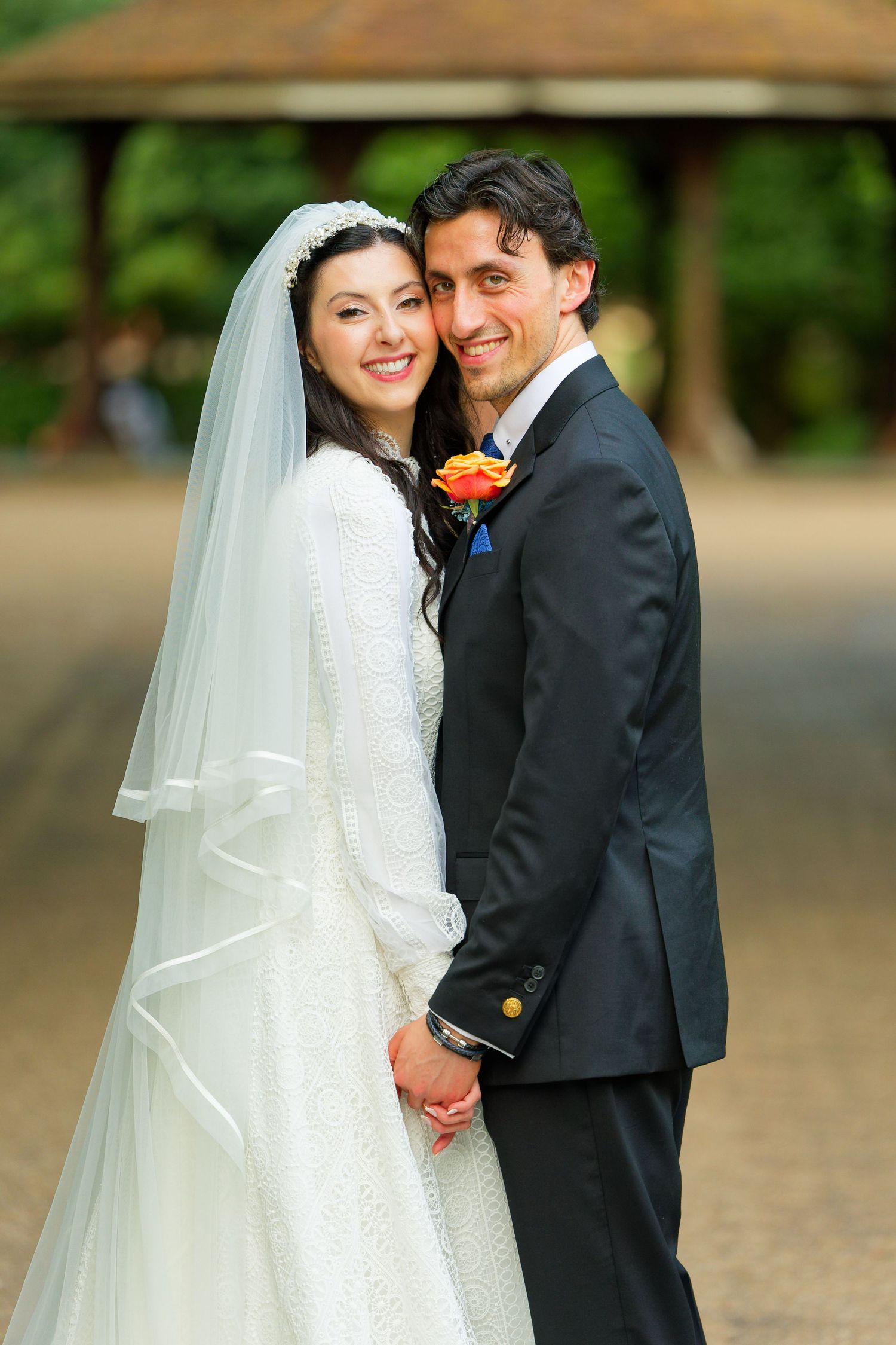 A bride and groom share an intimate moment outdoors while posing for wedding portraits in a garden setting.