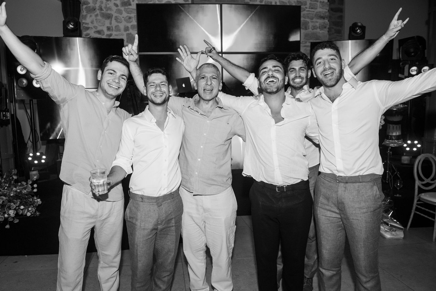 A black and white photo shows a group of friends celebrating with their arms raised in joyful celebration.