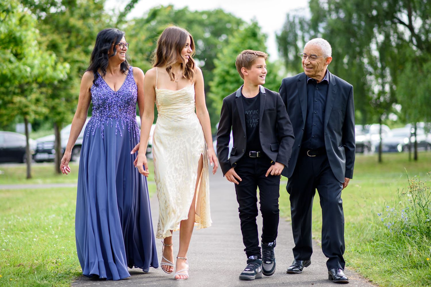 Wedding party in navy blue dresses and black suits walks along a garden path on a sunny summer day.