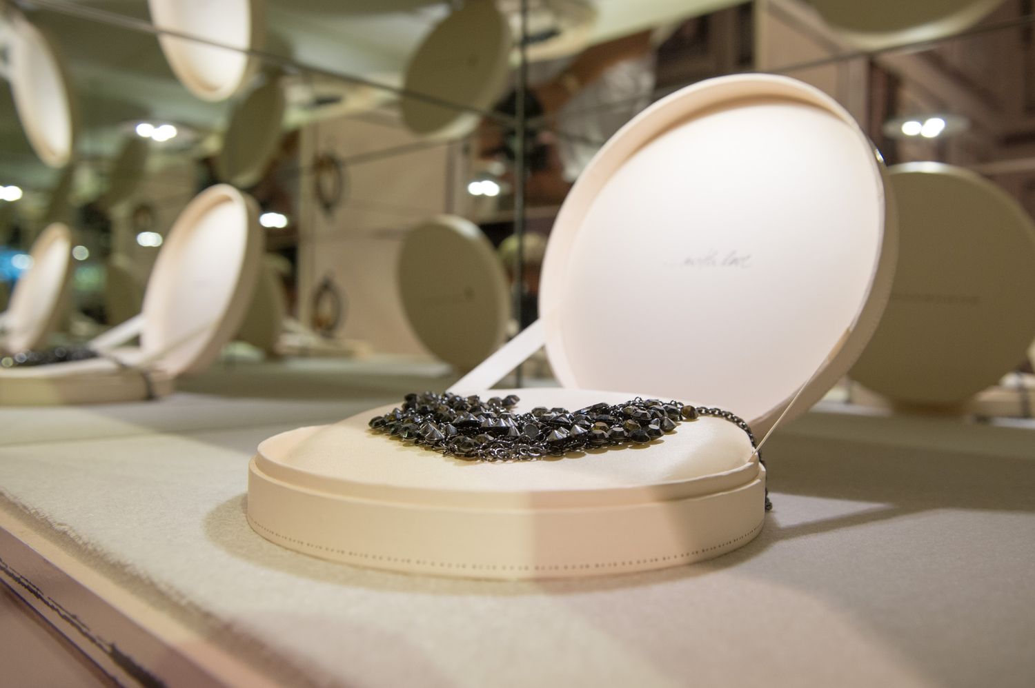 Luxury jewelry display featuring a black necklace on an elegant cream-colored presentation stand.