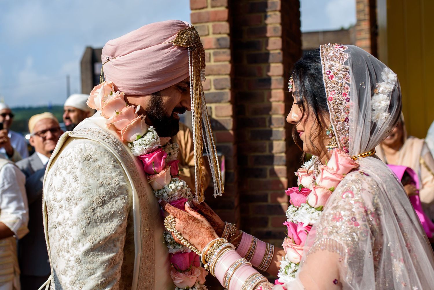 A joyful wedding celebration scene with people in traditional Indian attire and pink turbans at a brick venue.