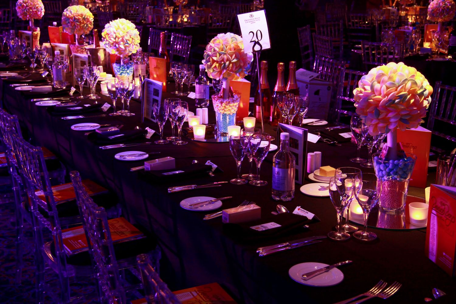 Elegant table settings with purple lighting and floral centerpieces at formal dining event.