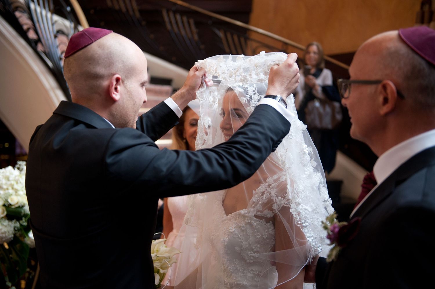 A bride and groom share their first kiss during a wedding ceremony while guests look on.