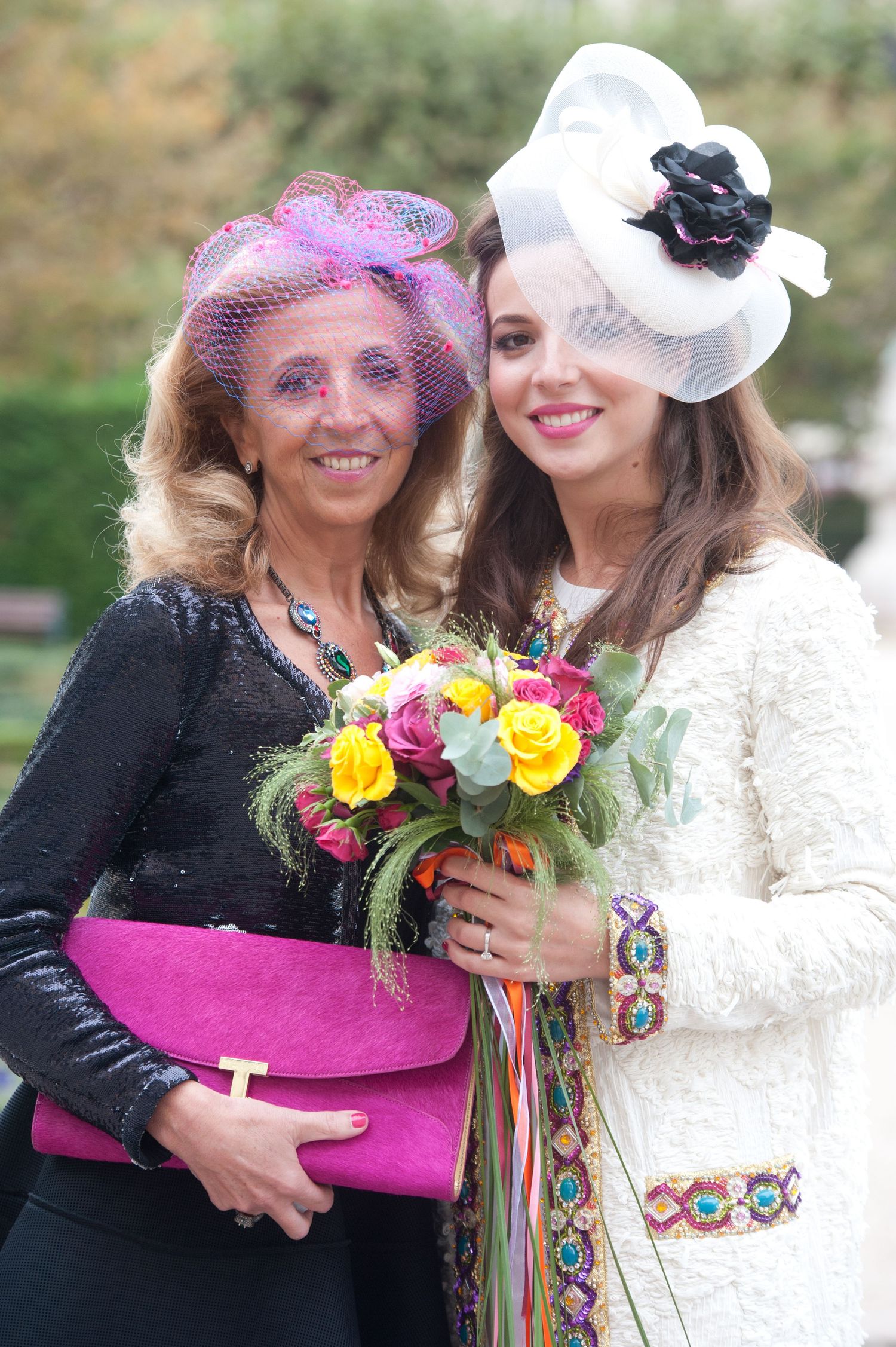 Two people in festive attire embrace while holding colorful bouquets at an elegant outdoor celebration.