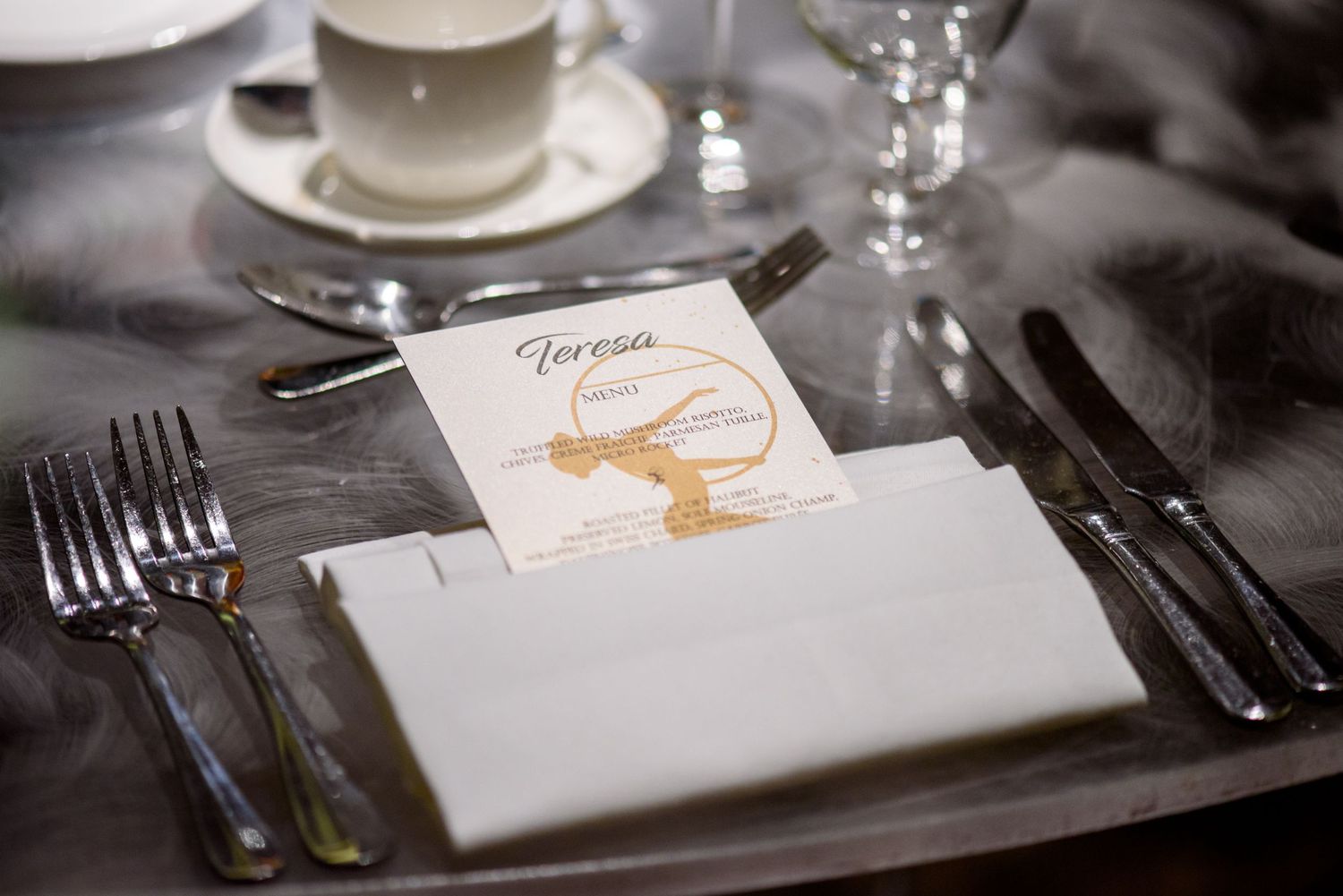 Formal place settings with white china, silverware, and elegant menu cards on dining table.
