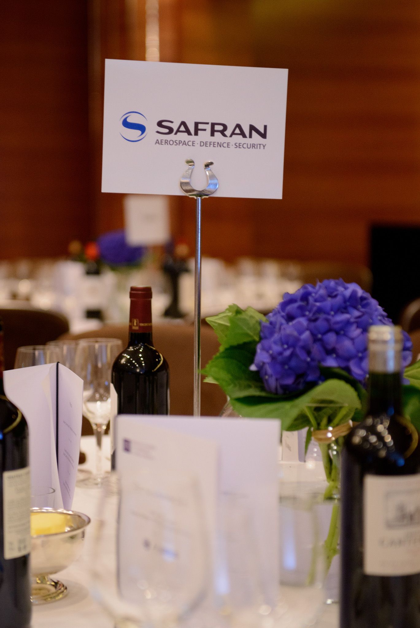 Formal table setting with Safran company sign, wine glasses and purple hydrangea floral arrangement.