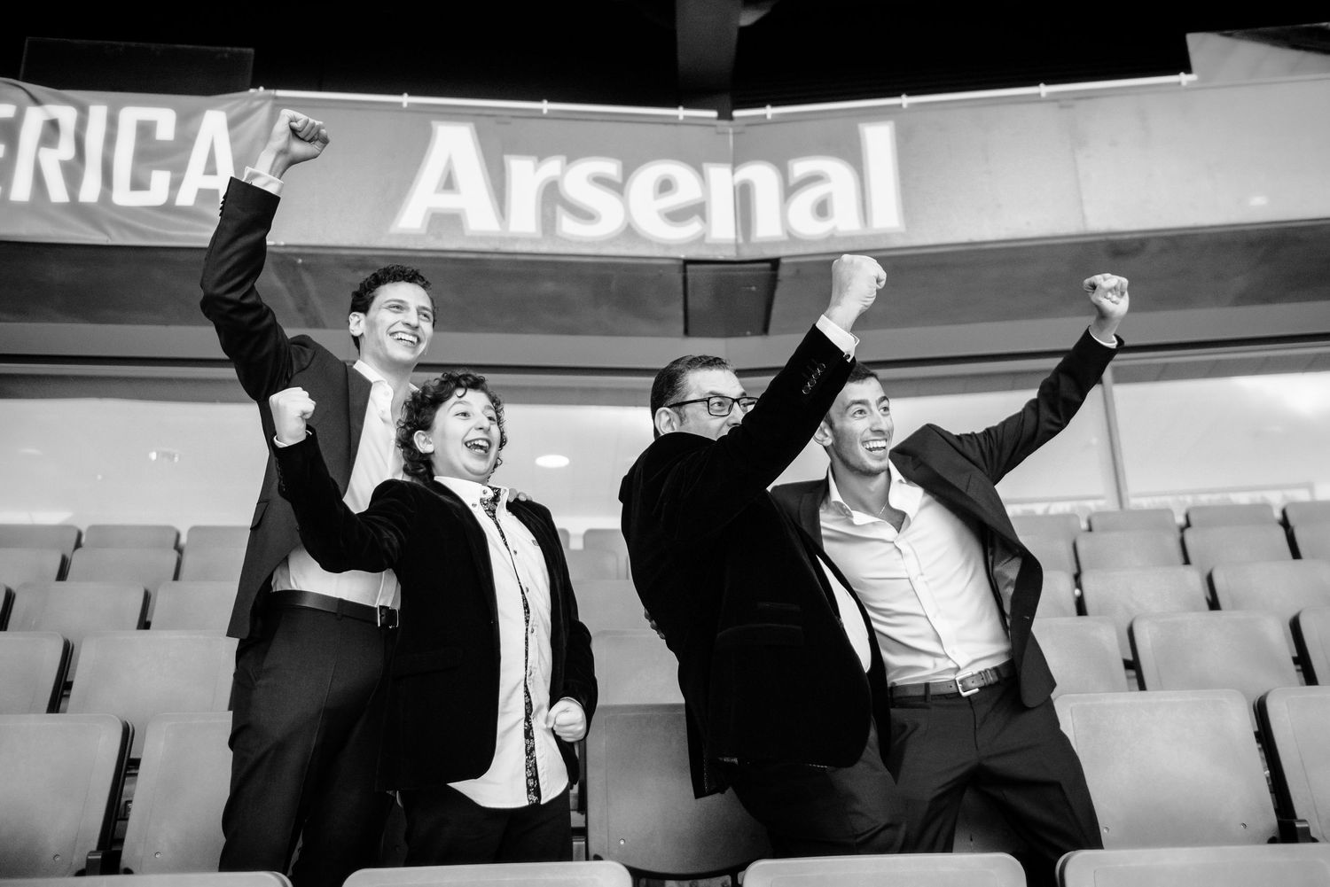 Black and white photo showing soccer fans celebrating in stadium seats during a match at Arsenal's home ground.