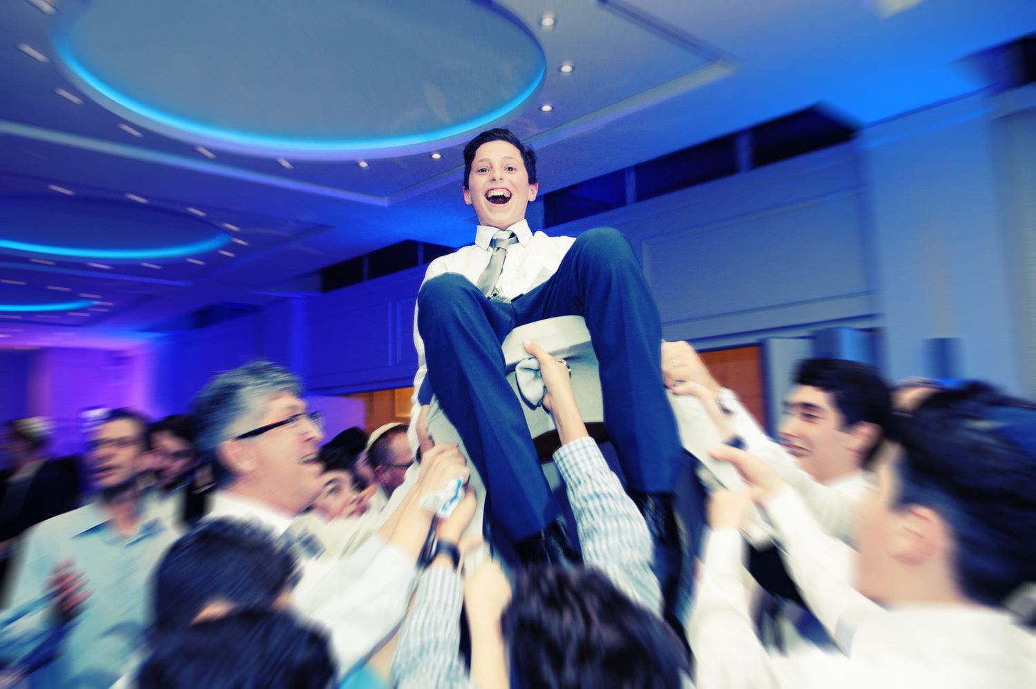 A crowd of people dancing and celebrating at a party with blue lighting and entertainment.