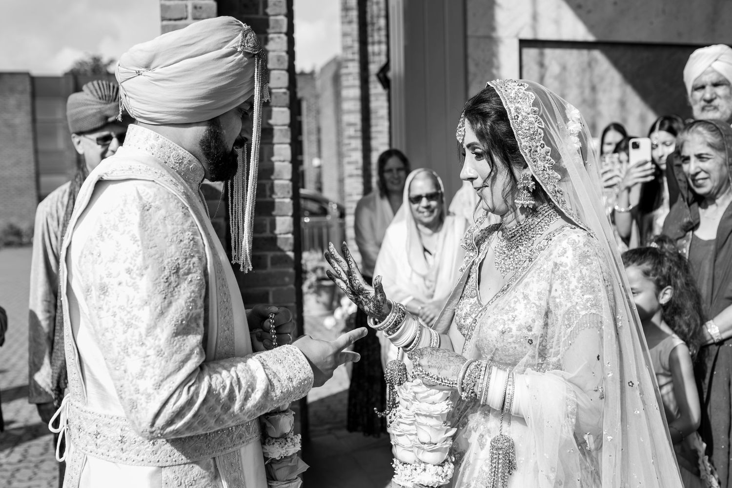 Black and white photo of a traditional Sikh wedding ceremony with the couple exchanging rings outdoors.