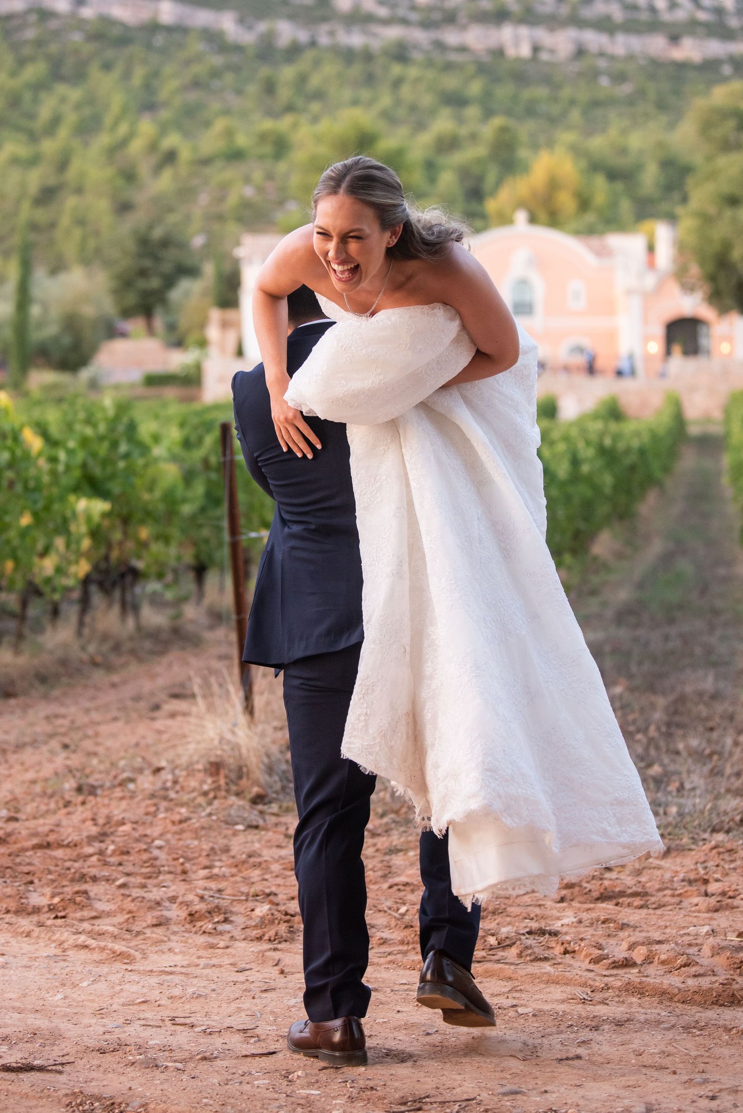 A couple shares a joyful moment at a vineyard wedding as the groom lifts the bride in her white dress.