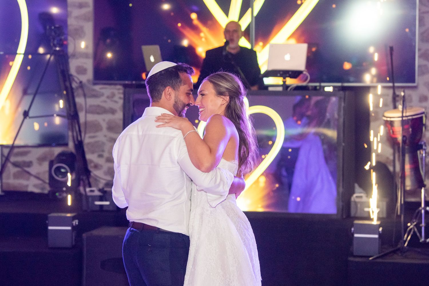 A couple shares a romantic kiss on a dance floor illuminated by colorful purple and white lights.