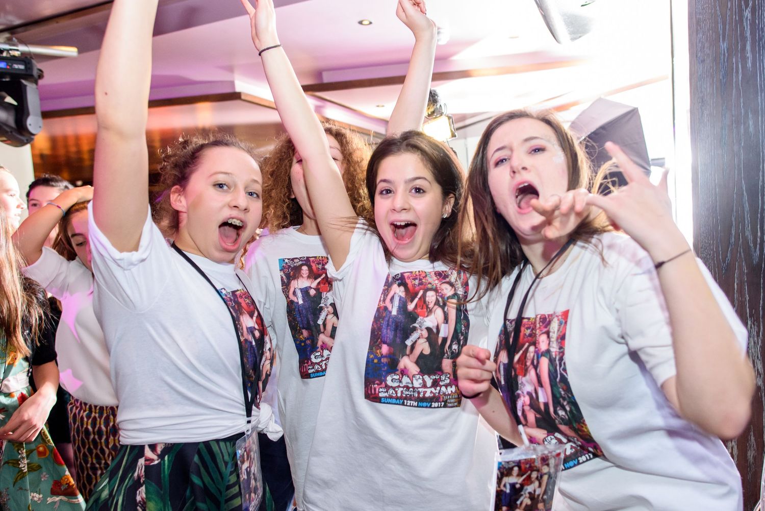 A group in matching white t-shirts reacts with excitement and celebration at an event.