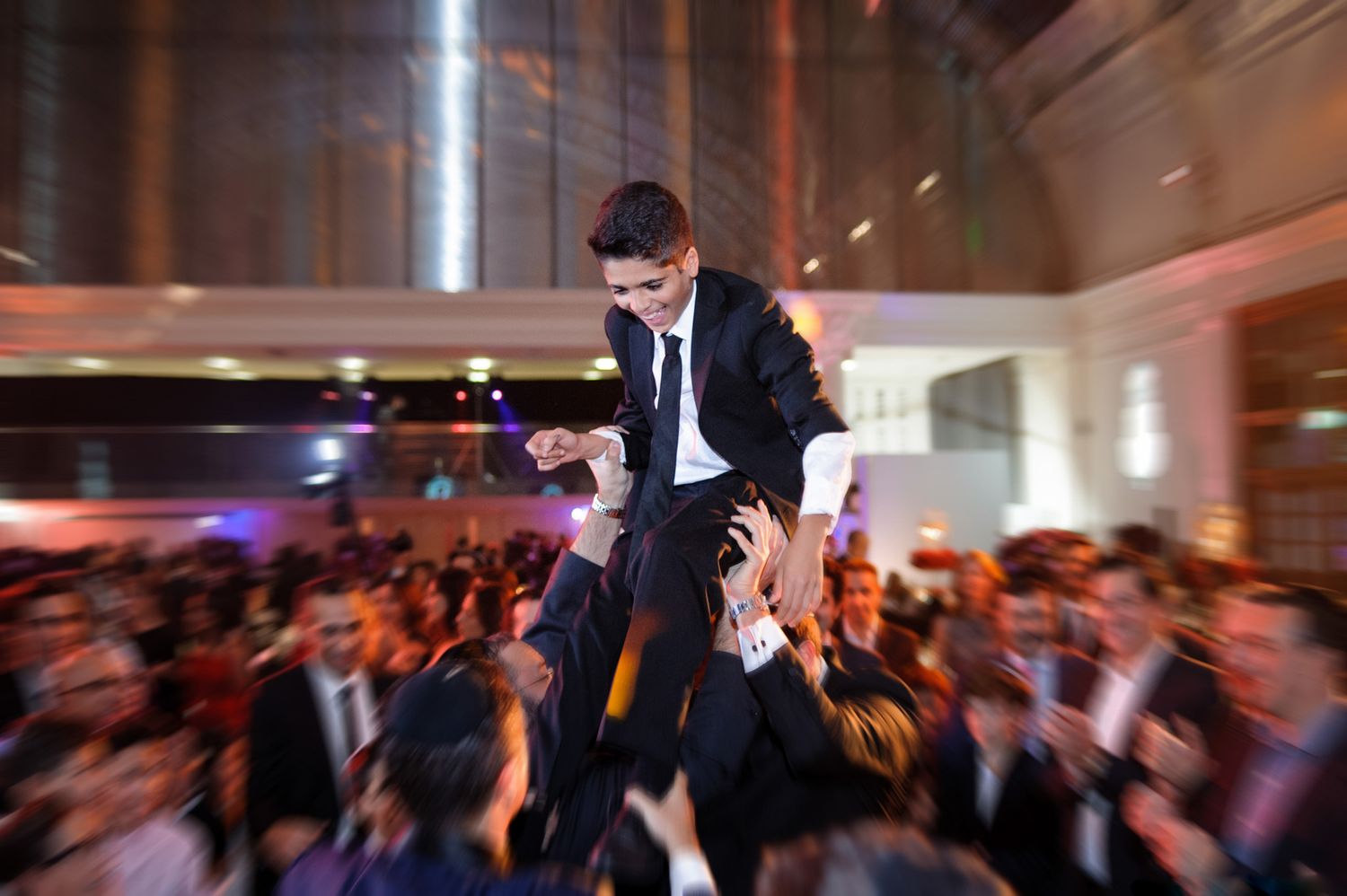 Wedding guests dance and celebrate on a crowded reception dance floor with colorful lighting and motion blur effects.