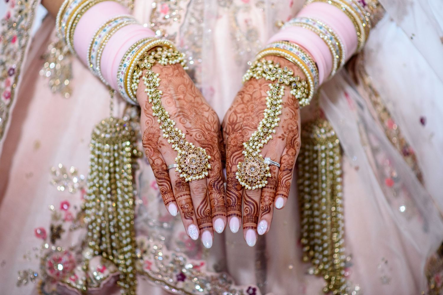 Traditional Indian bridal hands adorned with intricate henna designs and gold jewelry against pink attire.