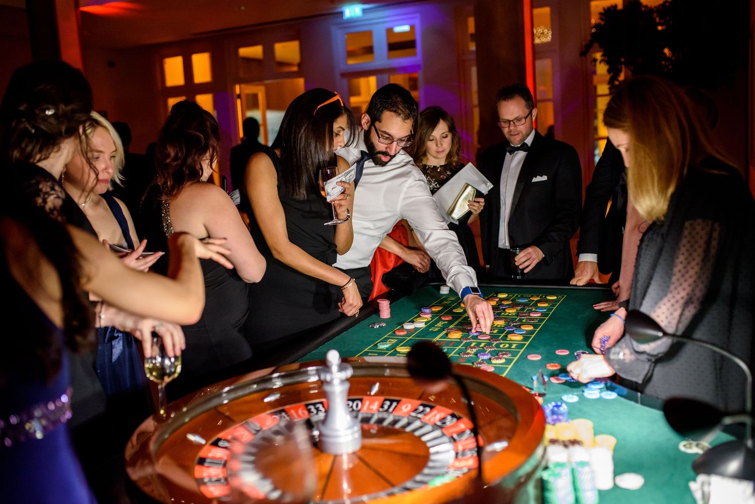 Roulette and gaming tables with players in formal wear at an evening casino event.