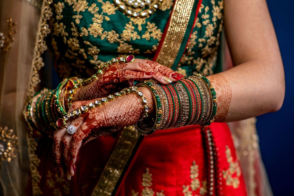 Indian bride showcasing intricate mehndi henna hands adorned with colorful bangles and gold jewelry.