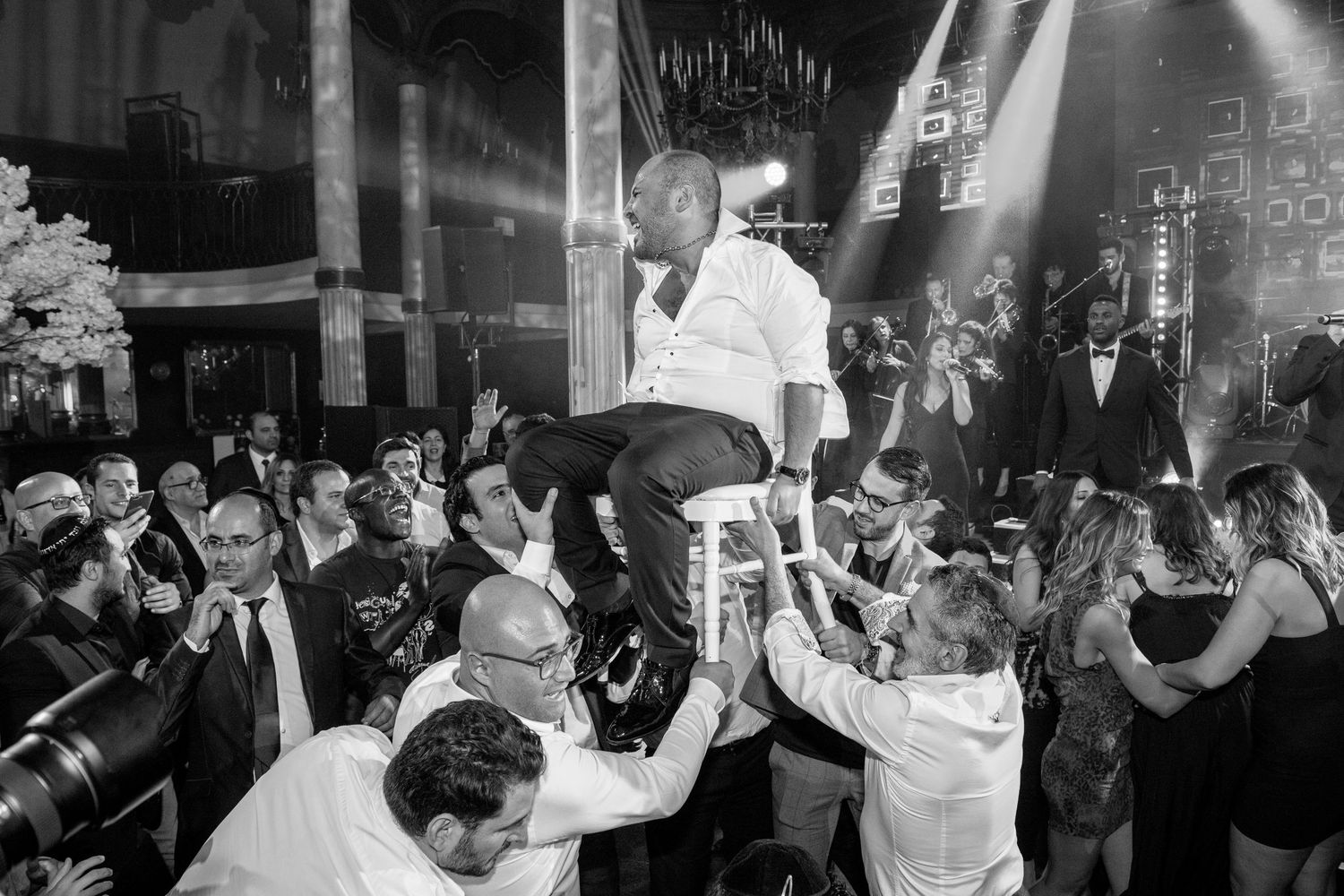 Wedding guests lift and celebrate during a lively black and white reception party scene.