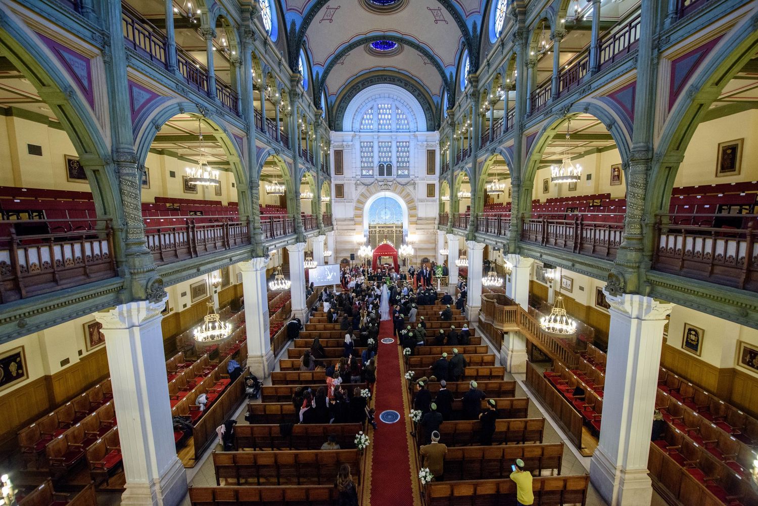 Interior view of a historic synagogue with ornate columns, arched ceilings, and wooden pews arranged in rows.