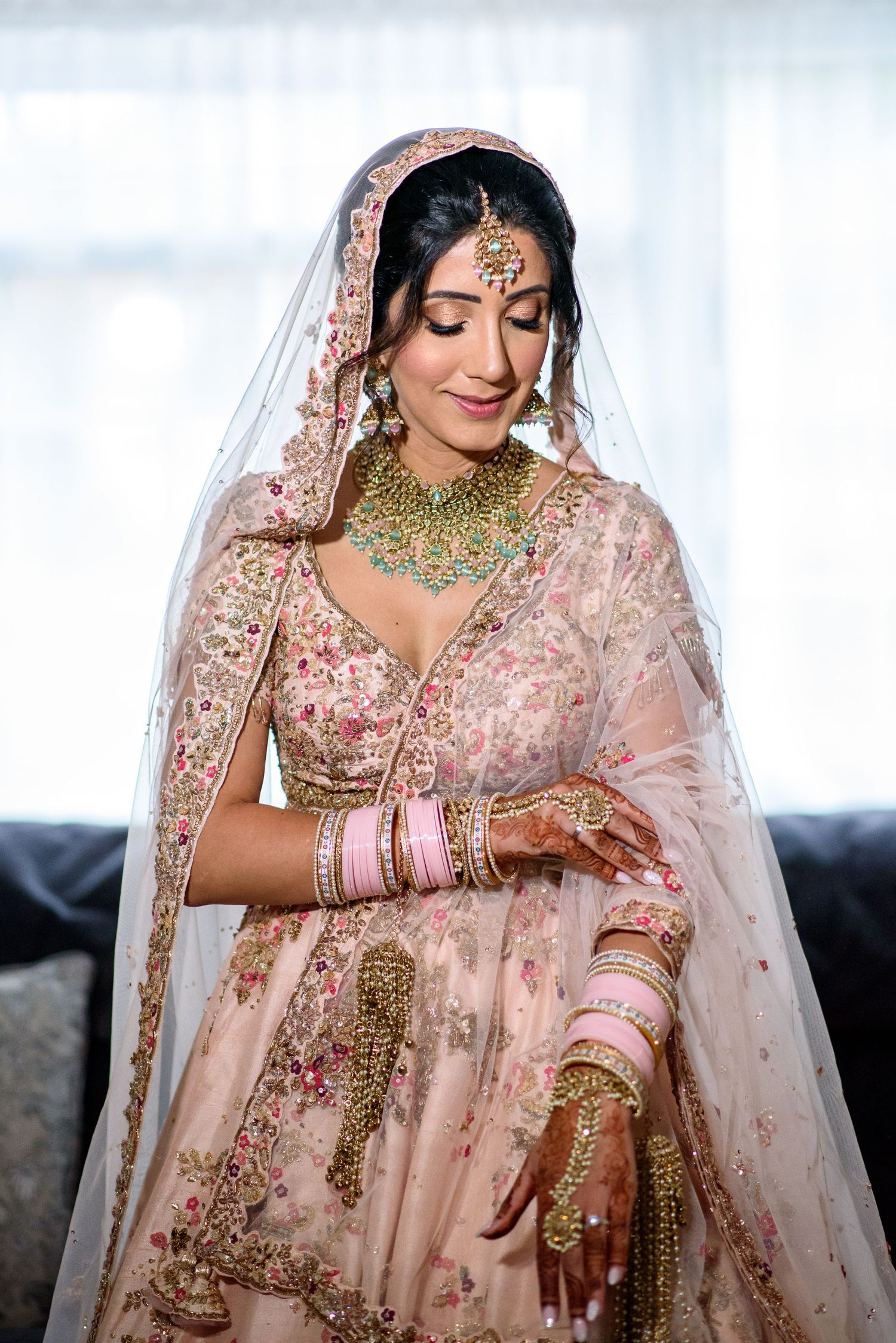A bride wearing a pink embroidered lehenga and traditional Indian bridal jewelry poses in multiple shots.