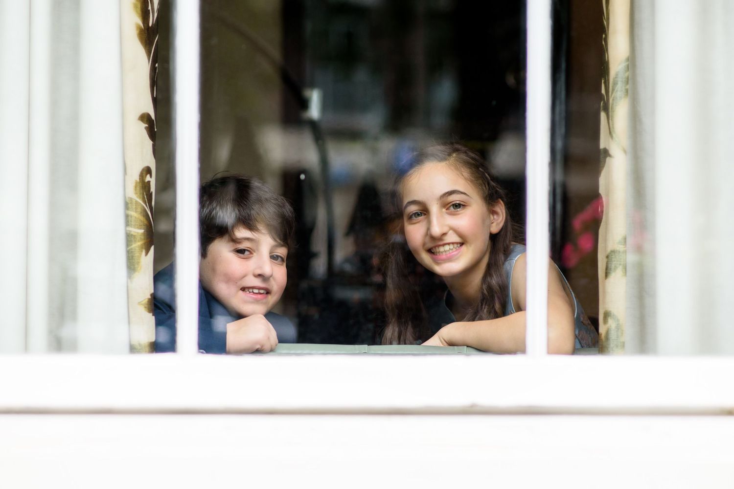 A row of smiling faces peering through a window with white frames and reflective glass.