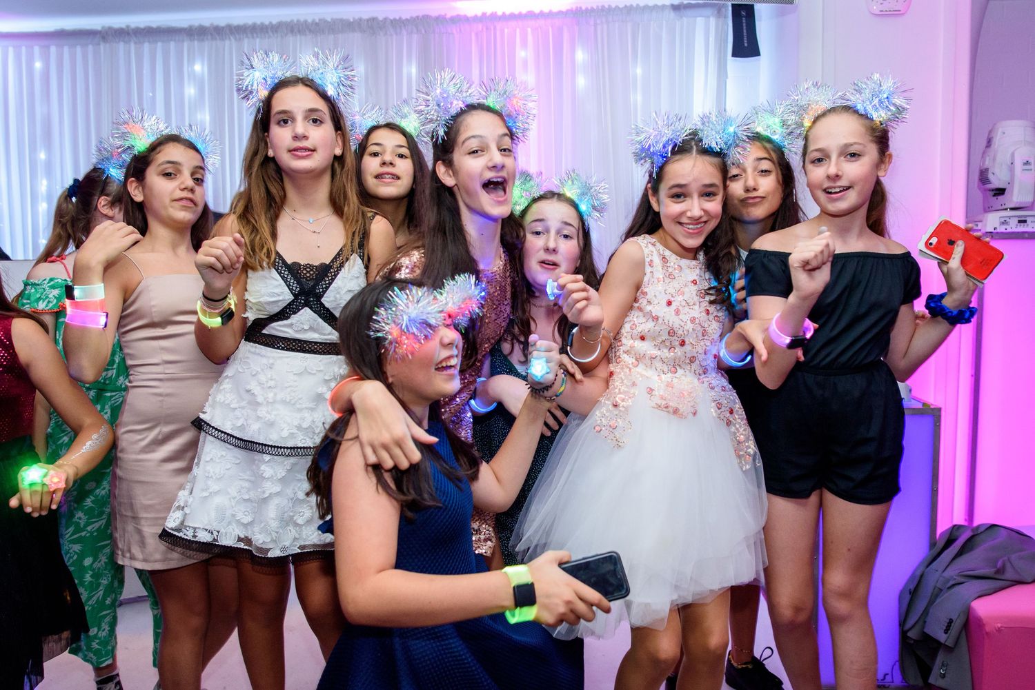 Wedding guests dance and celebrate together on a pink-lit dance floor at a reception party.