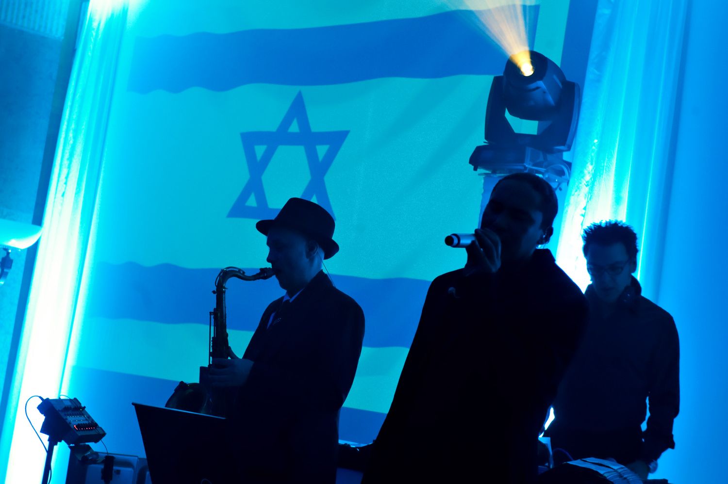 Silhouetted figures stand against a vibrant blue backlit stage during a live performance.