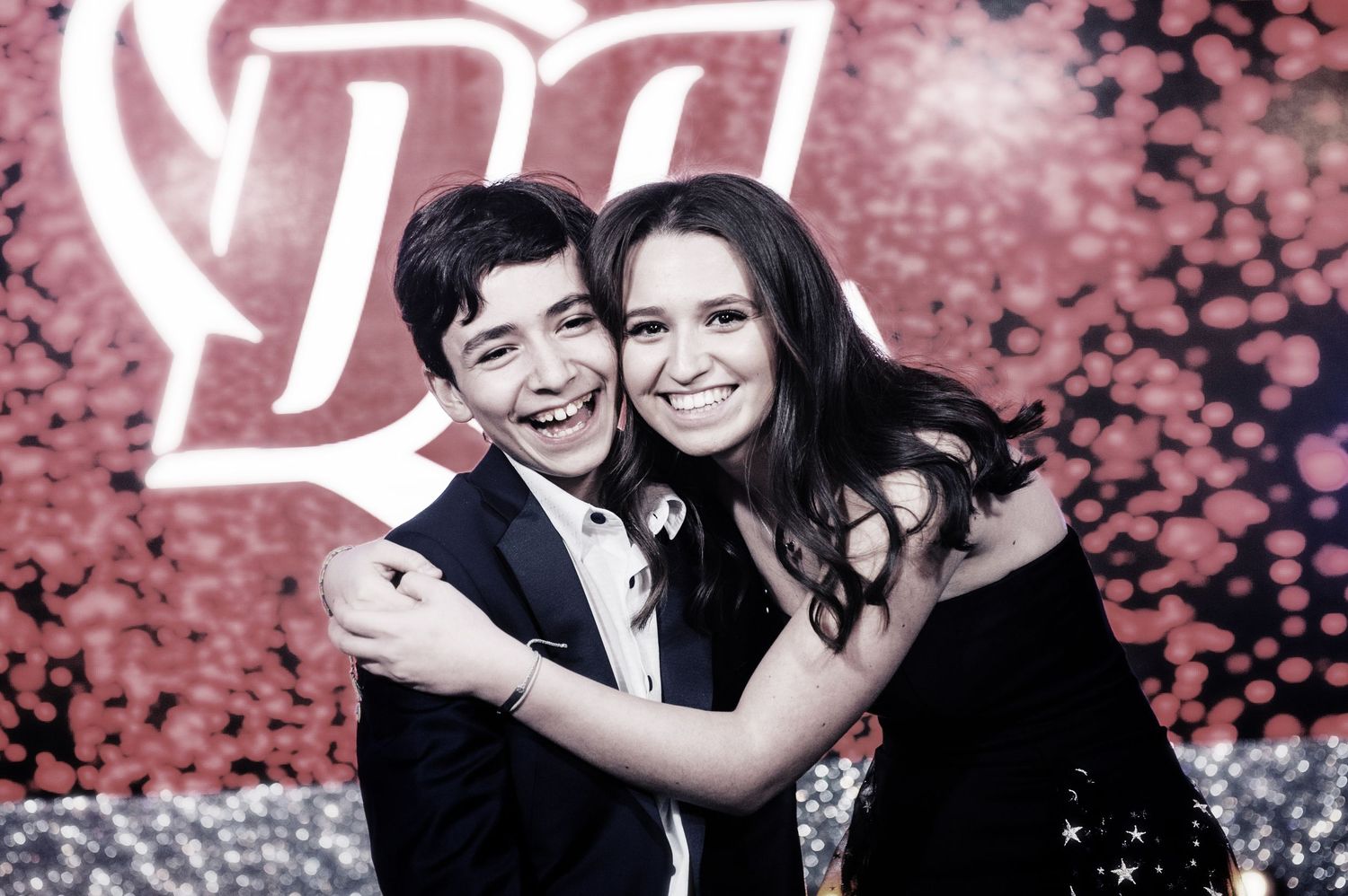 A couple poses together at a photo booth with pink and silver bokeh lighting effects in the background.