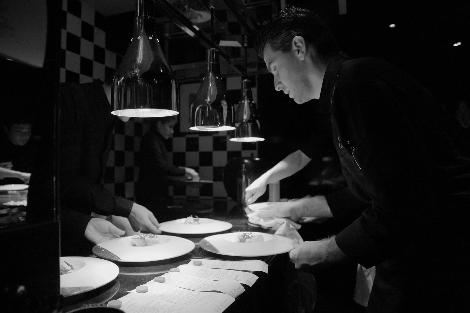 Restaurant staff working in a dimly lit kitchen with checkered walls.