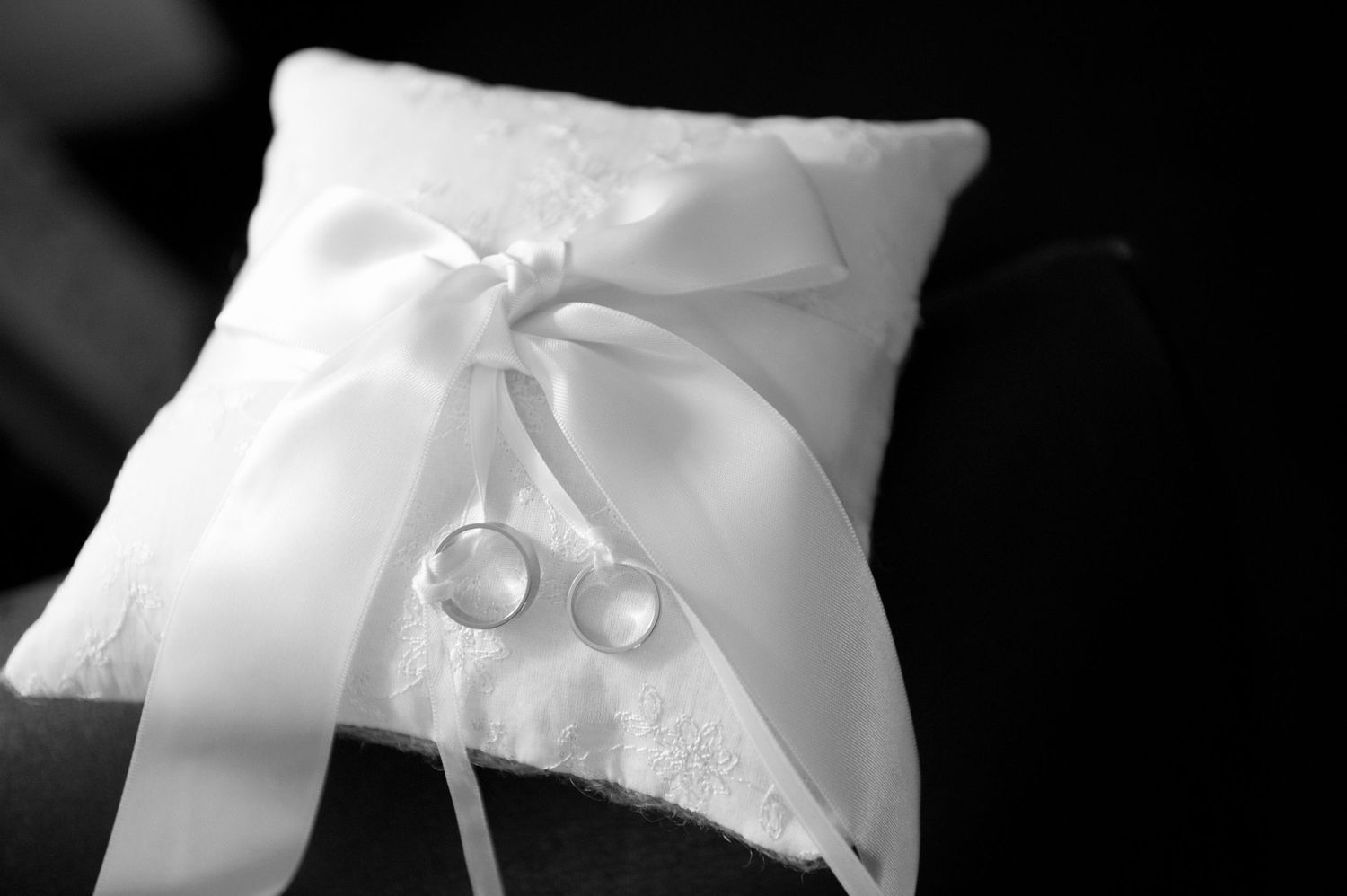 Close-up view of white satin ring bearer pillows with decorative ribbons and bows.