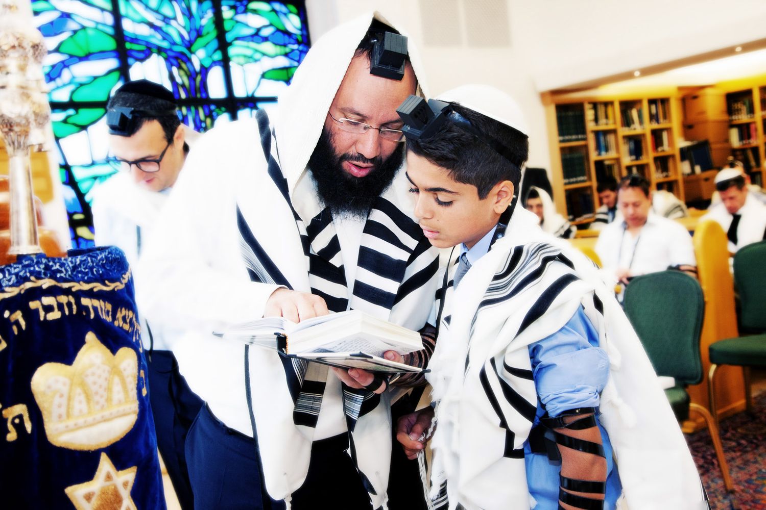 Jewish men praying together in synagogue while wearing traditional white prayer shawls and tefillin.