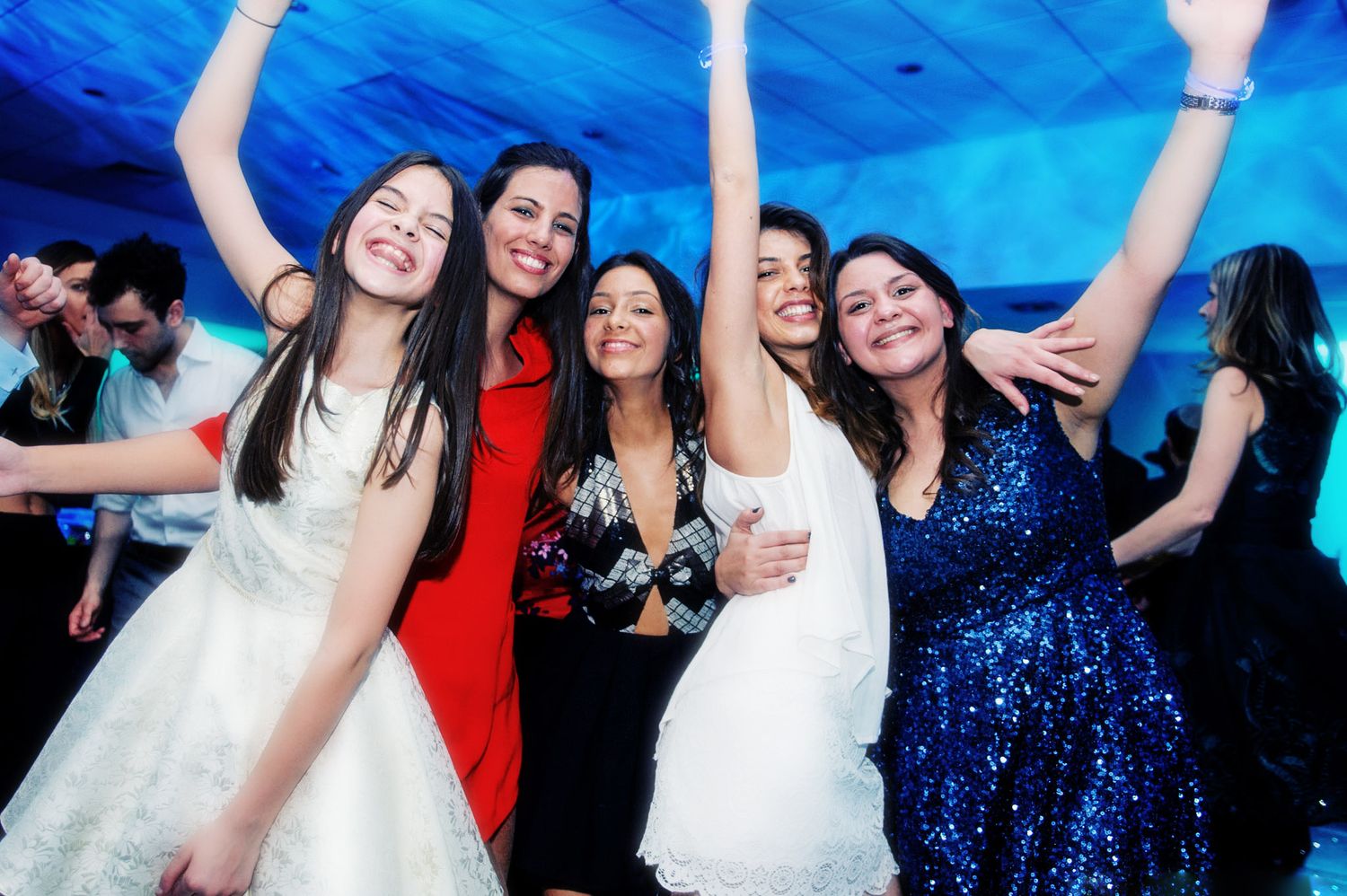 A group of people dancing and celebrating at a festive party with blue lighting and sparkly dresses.