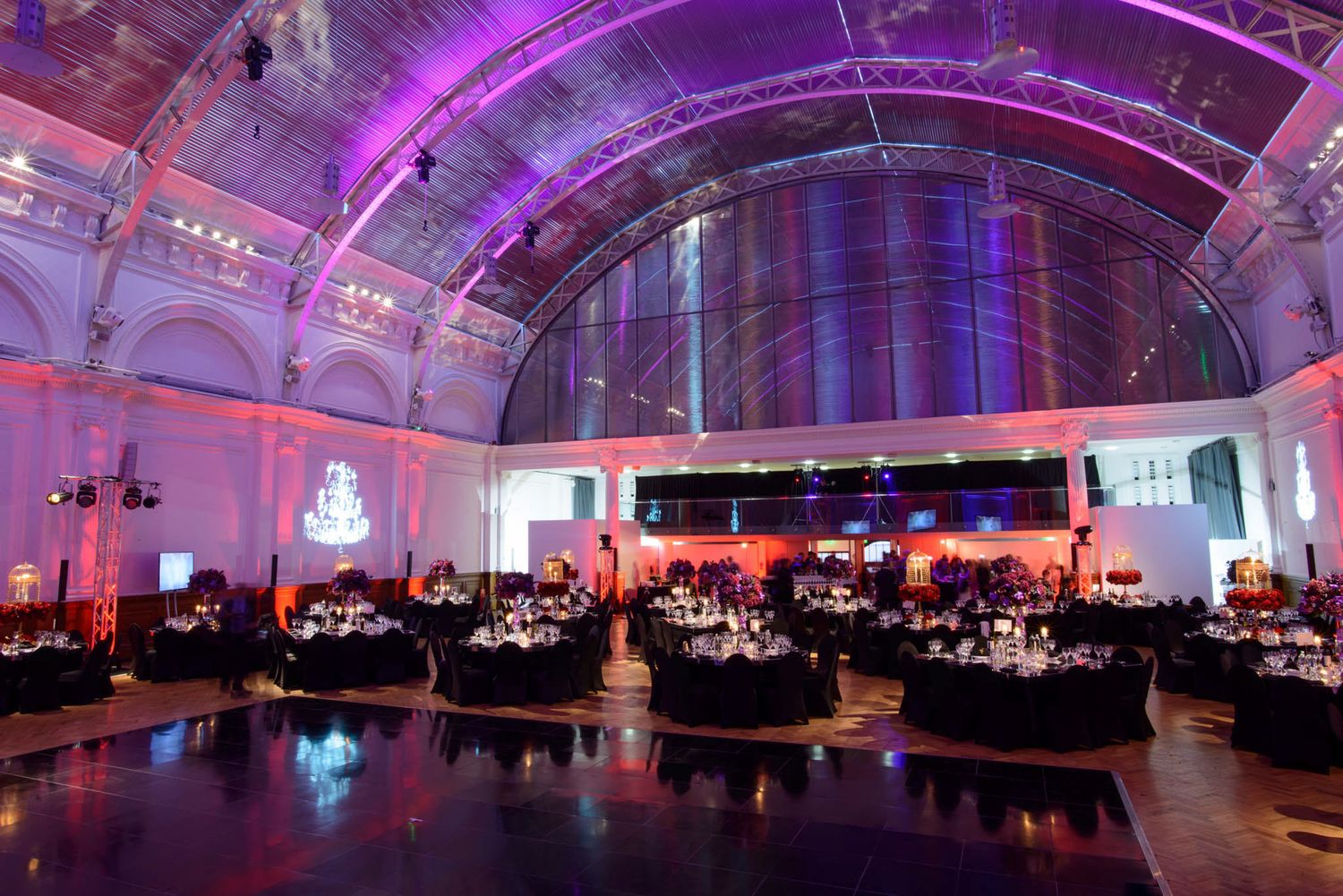 Large event venue with purple and red lighting illuminating tables and decor for an elegant indoor celebration.