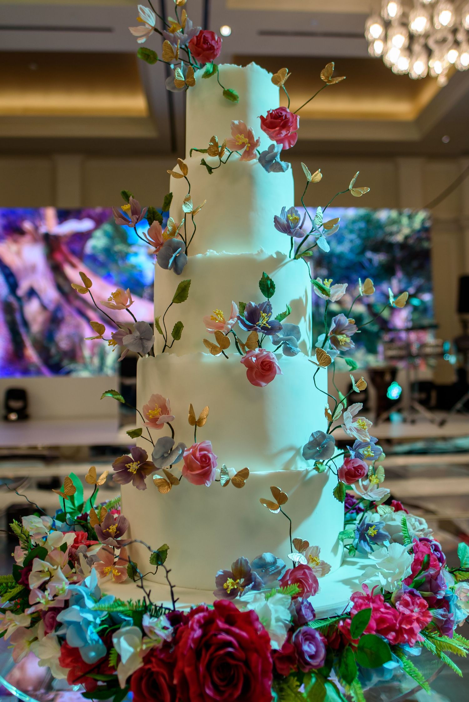 A wedding cake decorated with cascading pink and red roses and turquoise lighting creates an elegant display.