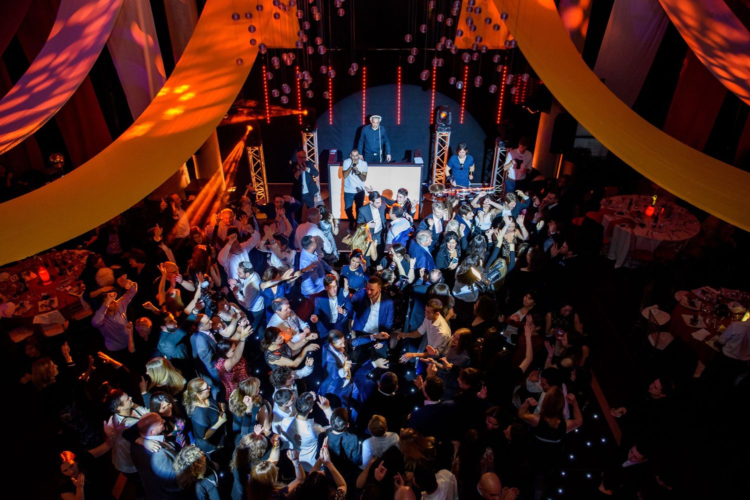 A crowded nightclub dance floor illuminated with vibrant orange and blue lighting during a lively party.
