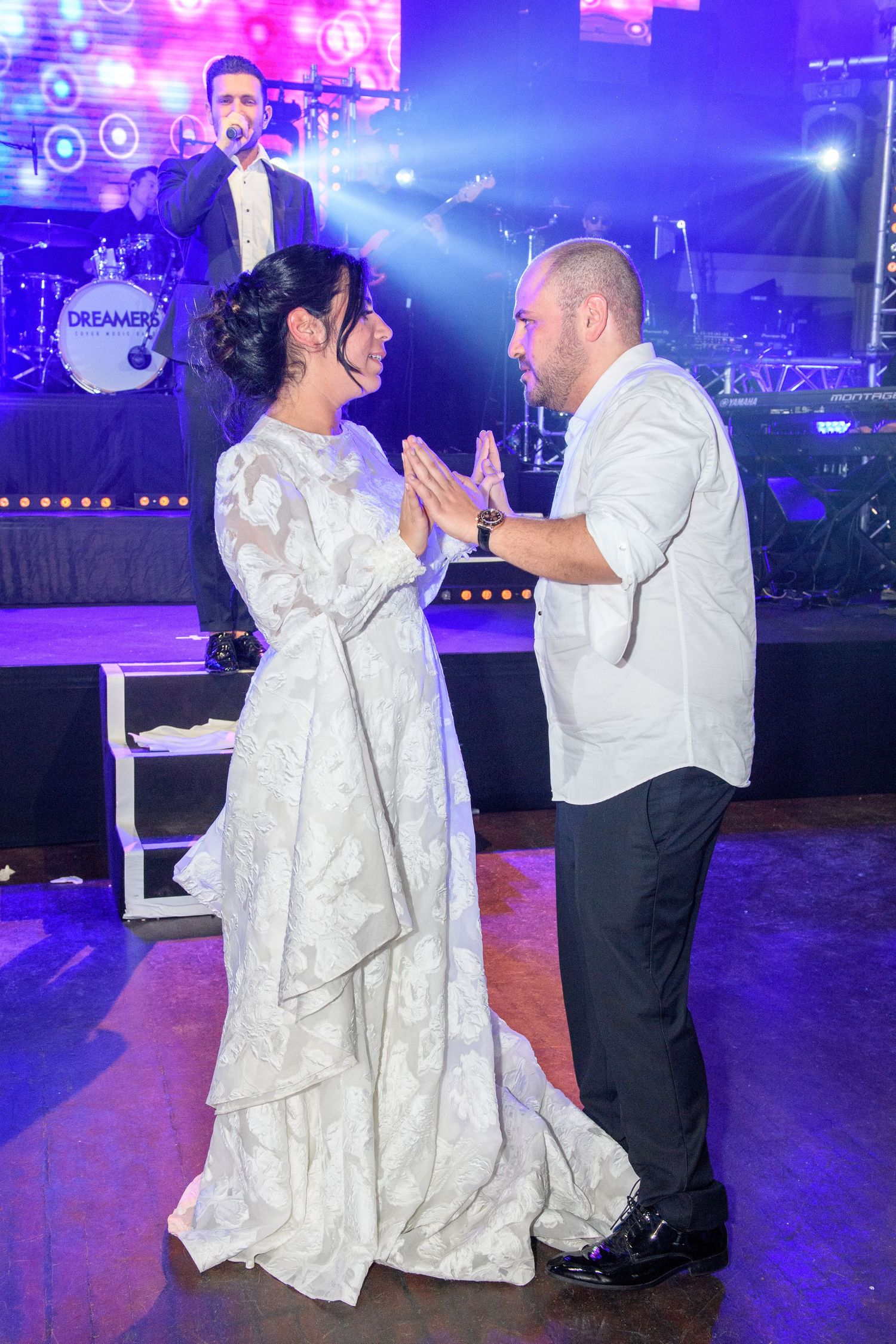 A couple in formal attire dances together at a wedding reception with blue and purple lighting in the background.