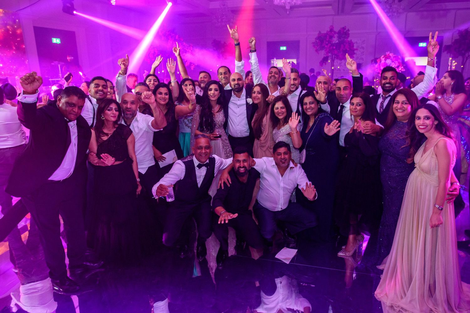 Wedding reception dance floor filled with guests celebrating under vibrant purple lighting at an indoor venue.