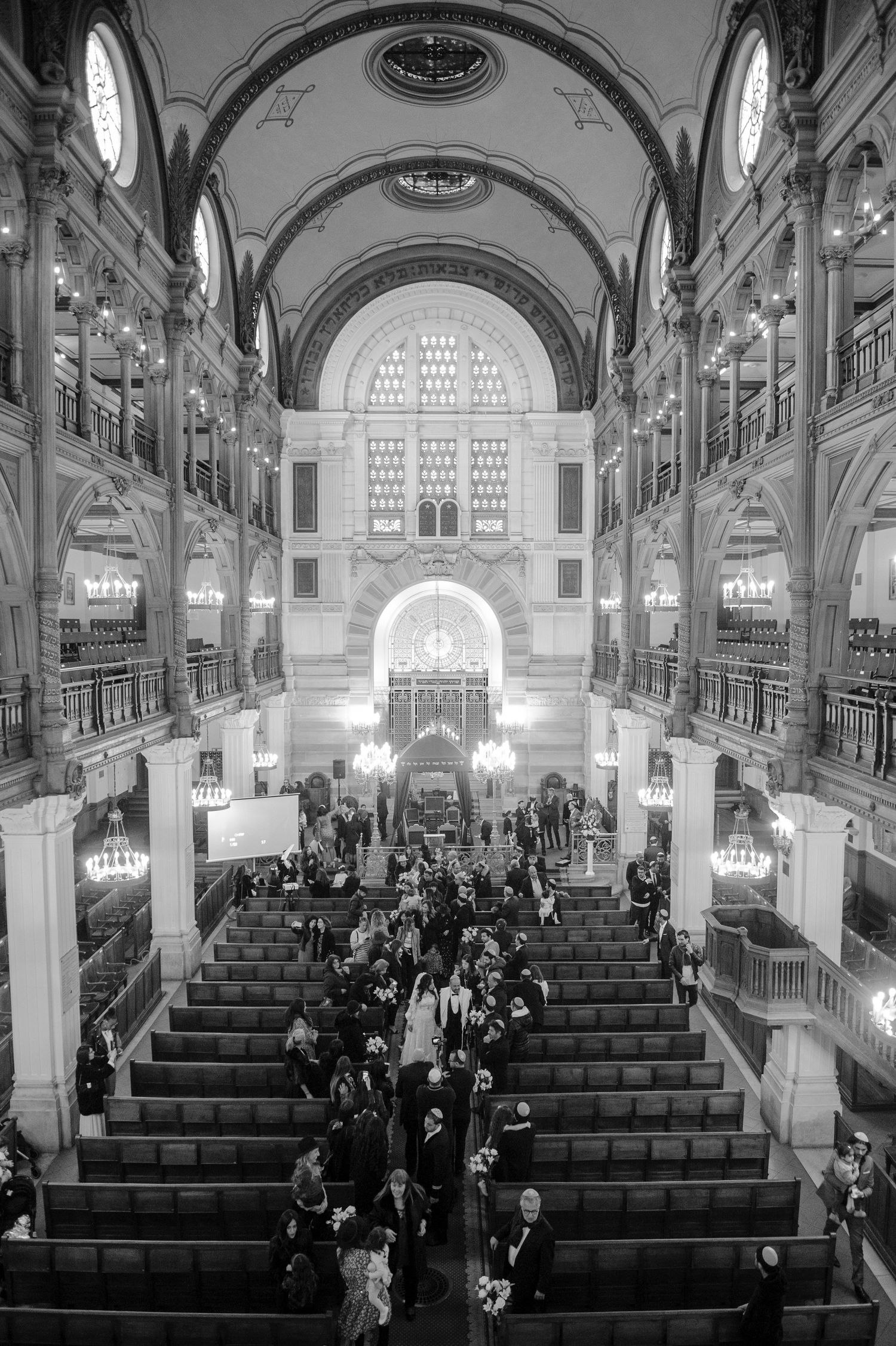 Interior view of a historic synagogue with arched ceilings and ornate architecture as people gather in the pews.