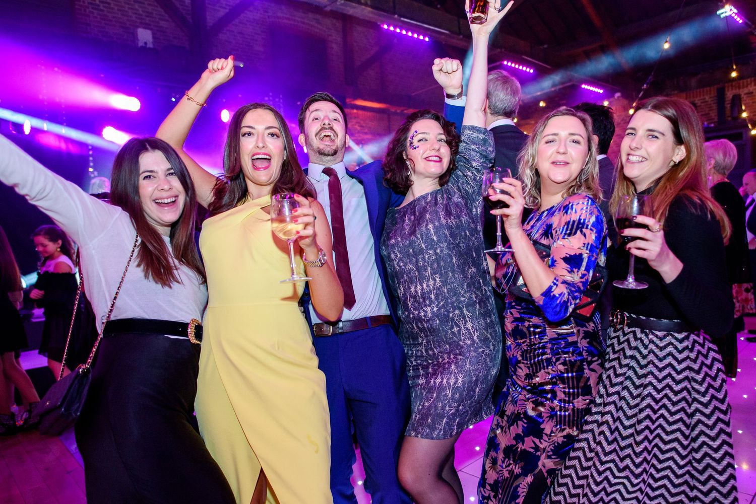 A group of people dancing and socializing at a nightclub with purple lighting and party atmosphere.
