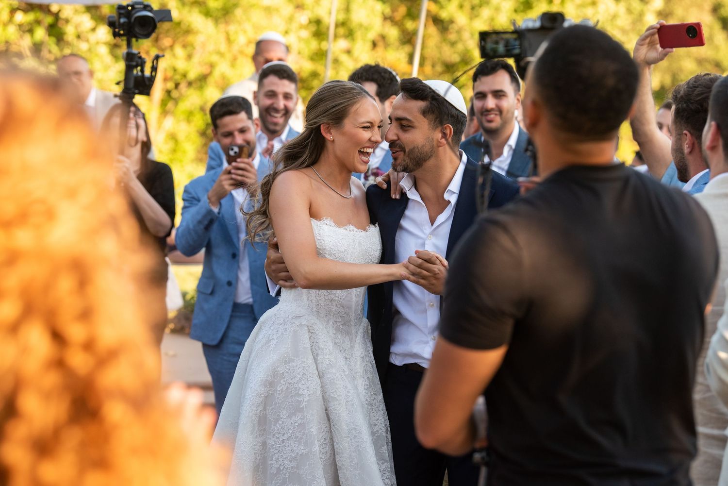 Wedding guests celebrate and dance together during an outdoor reception with golden sunset lighting.