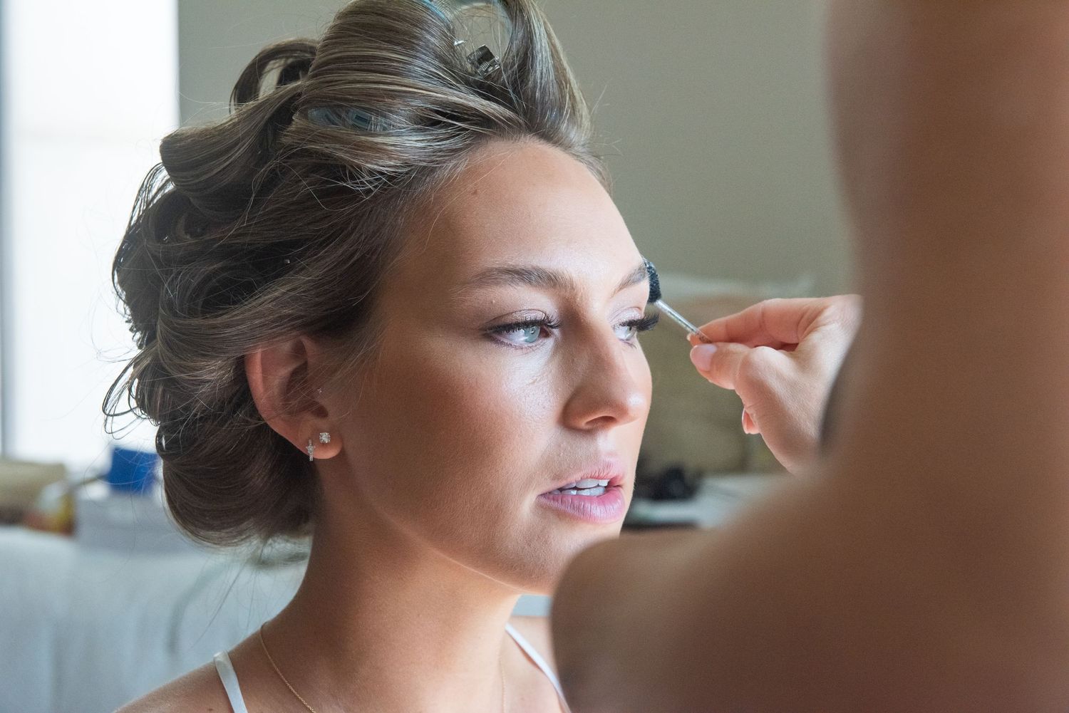 Final touches of makeup being applied during bridal preparation with soft natural lighting.