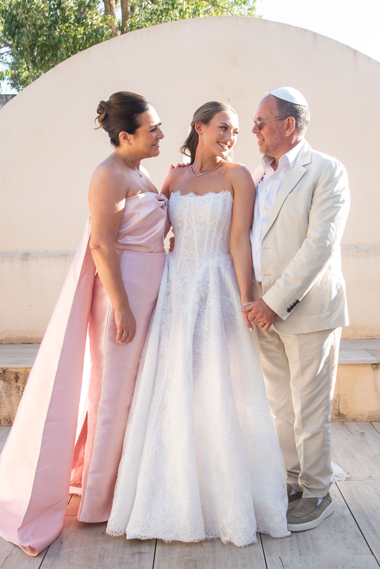 Wedding party members in light pink dresses and beige suit pose together on a sunny outdoor terrace.