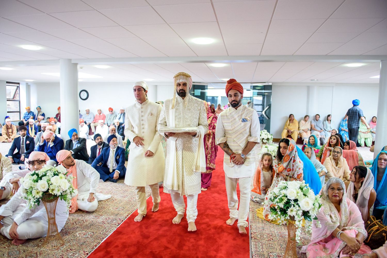 Wedding guests dance and celebrate during a lively reception in a bright indoor venue.