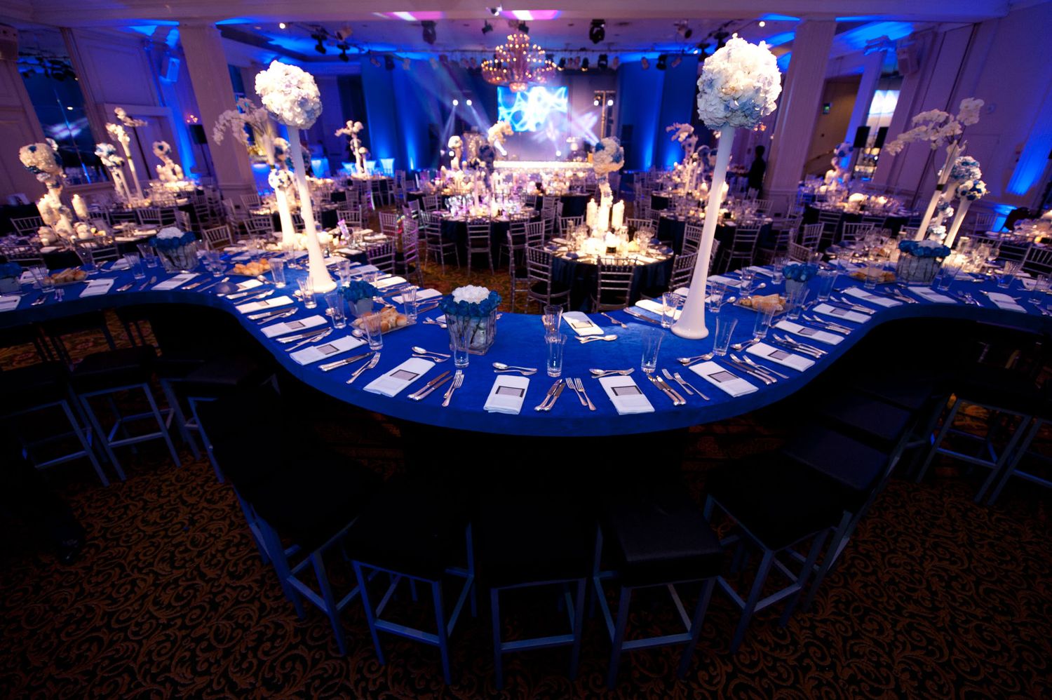 Elegant wedding reception venue decorated with dramatic blue uplighting and white table settings creates a magical atmosphere.