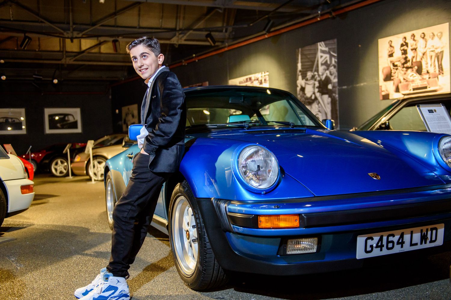 A bright blue classic Porsche 911 sports car is displayed in a dimly lit indoor showroom or garage space.