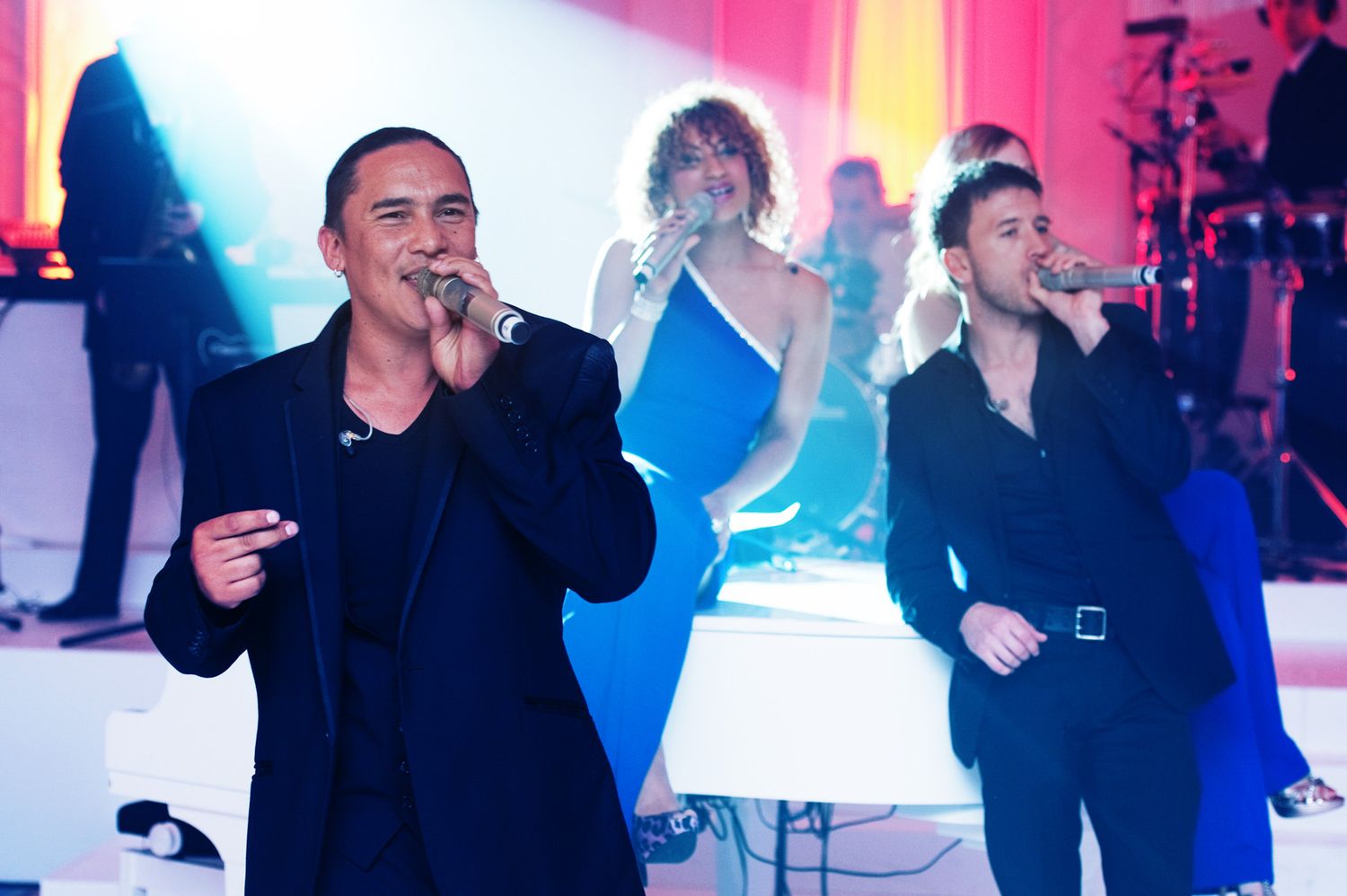 Performers entertain a crowd at a nightclub event with vibrant pink and blue lighting effects.