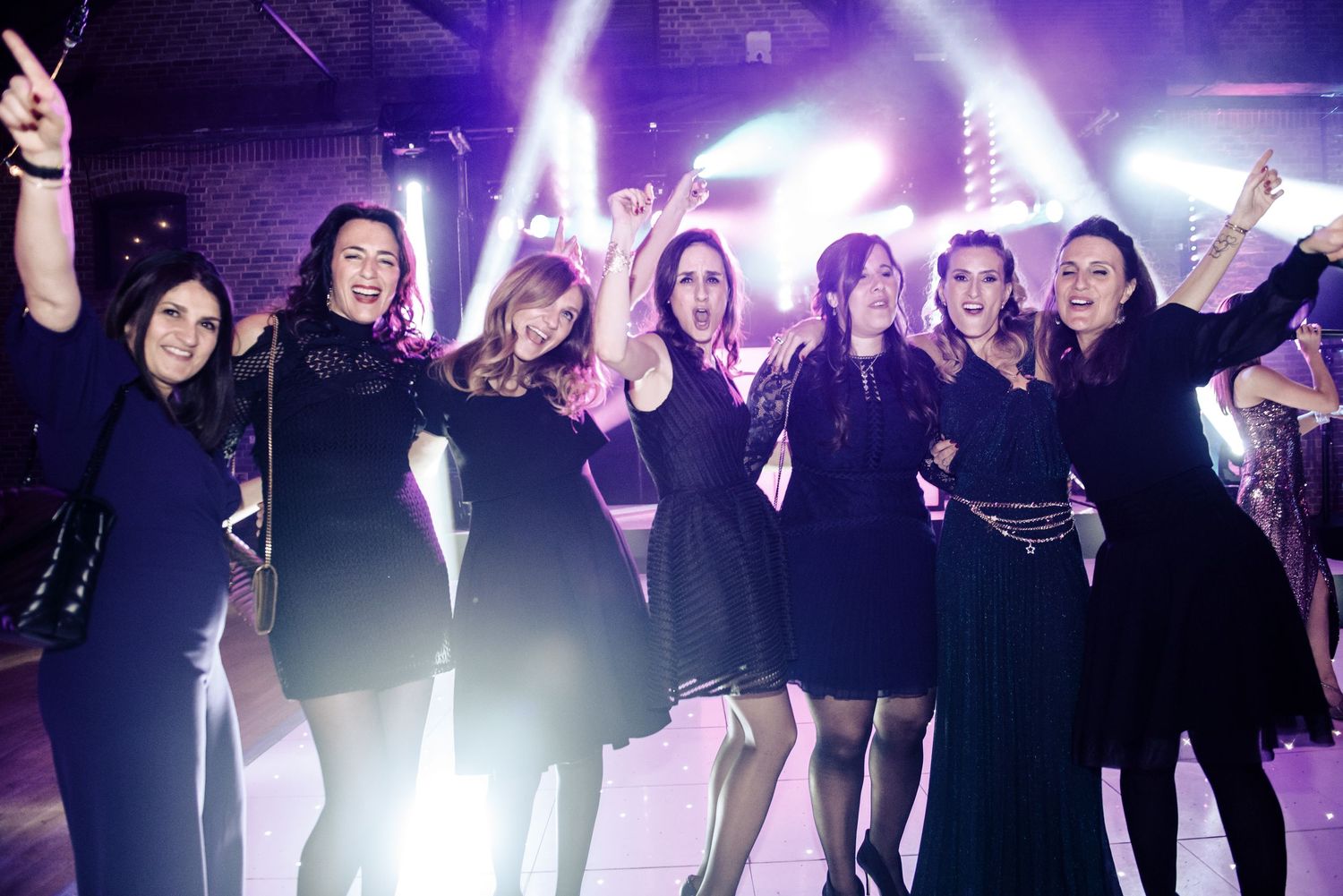 A group of performers in black outfits dance on stage with dramatic purple lighting effects in the background.