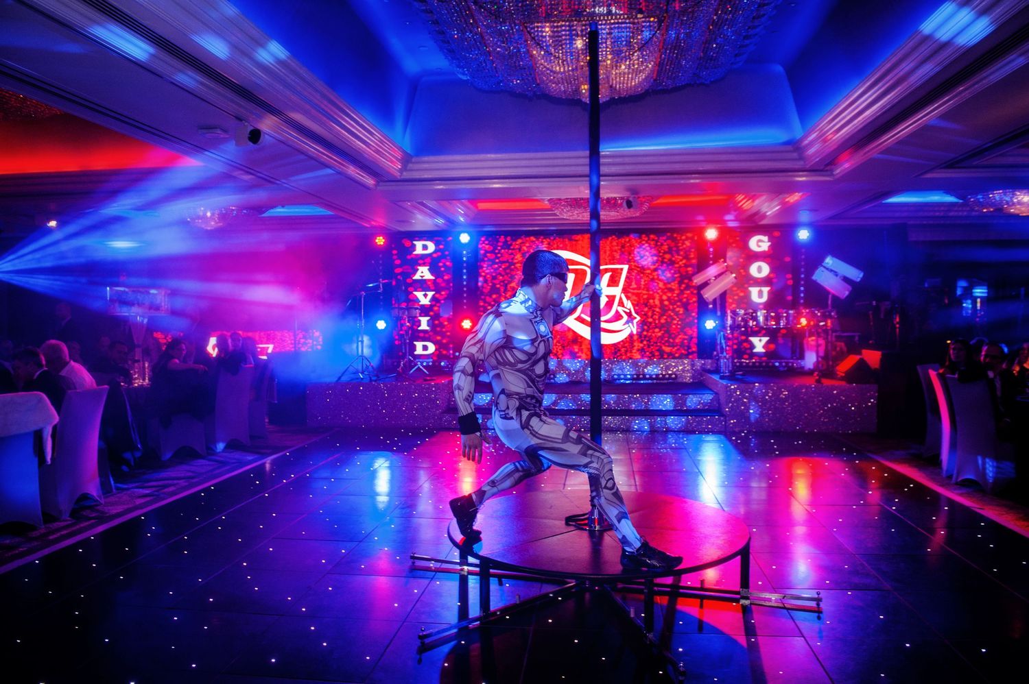 Colorful blue and red LED lights illuminate a large ballroom venue with dramatic ceiling and dance floor lighting effects.