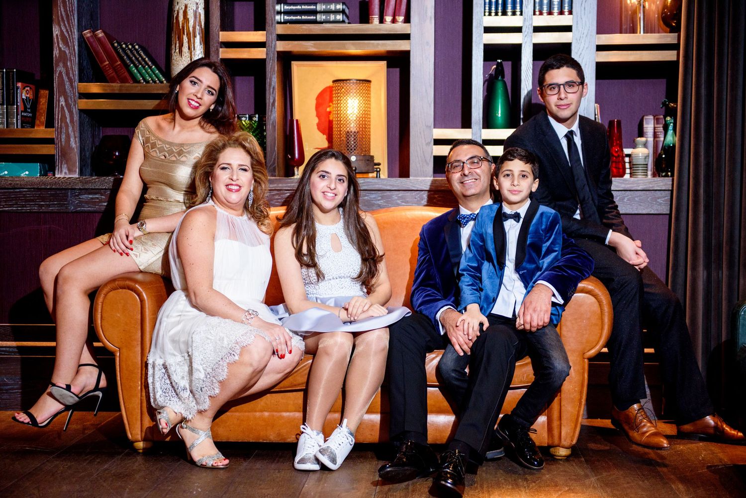 Wedding party members relax and socialize together on vintage leather couches during reception celebration.