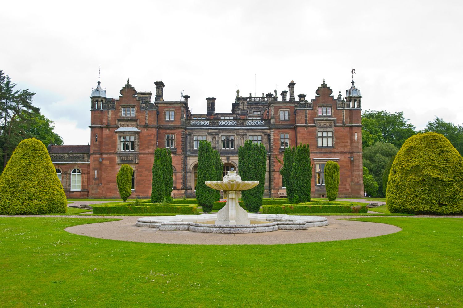 Panoramic view of a historic mansion with manicured gardens and central fountain.